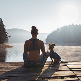 woman meditating neat the water on a lake with a dog