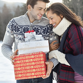 Couple walks in the snow holding holiday gifts